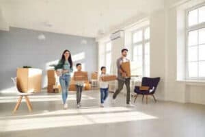 una famiglia composta da genitori e 2 bambini che portano pacchi e una piantina portata dalla mamma all'interno di un'ampio salone con qualche sedia e qualche scatolone.