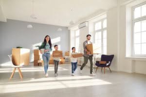 una famiglia composta da genitori e 2 bambini che portano pacchi e una piantina portata dalla mamma all'interno di un'ampio salone con qualche sedia e qualche scatolone.